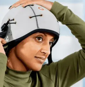 A young woman fitting a Paxman Cold Cap on her head in a doctor's office.