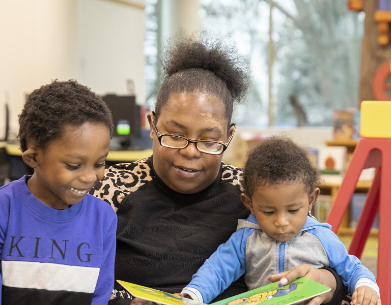 A mother reads to her two young children in a library.