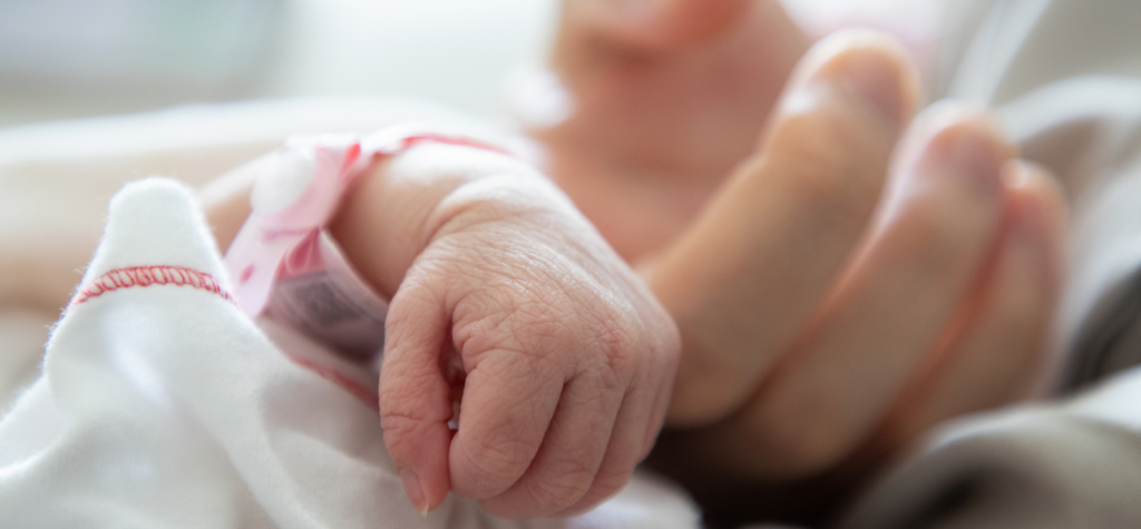 A newborn infant's hand wrapped around an adult's finger.
