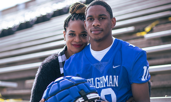 A teenage football player sits on the bleachers with his mother hugging him.