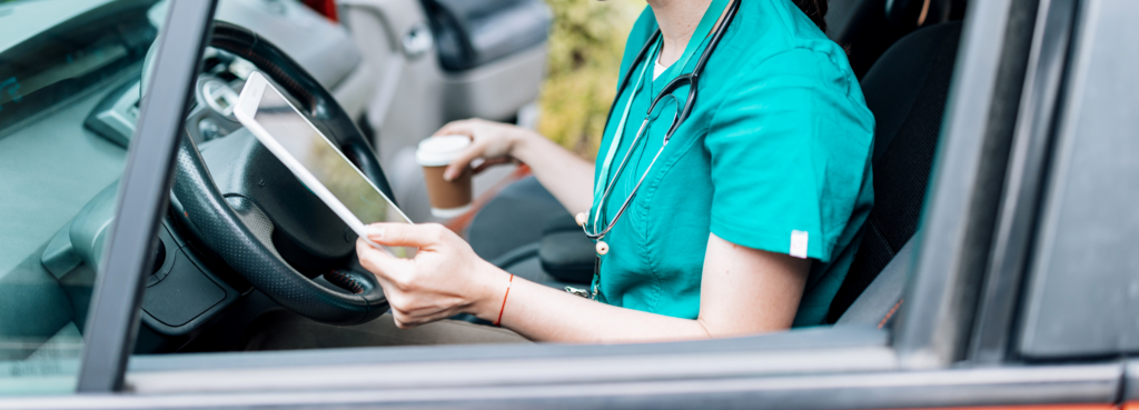 A nurse checks appointments on a tablet while inside a mini van.