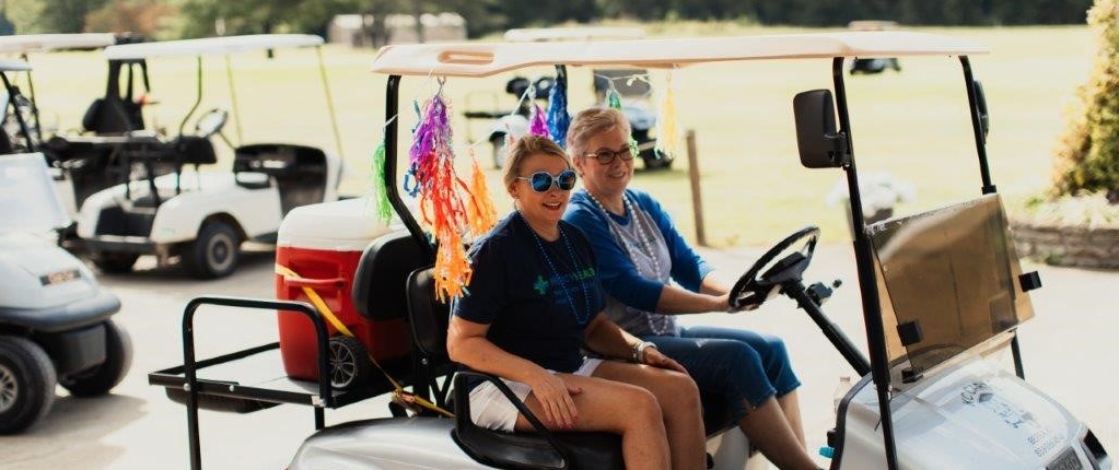 Two women cruise on a golf cart at Mercy Health Foundation Irvine's Annual Golf Scramble.