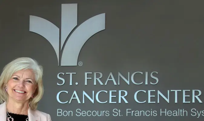 An elderly woman smiles while standing outside Bon Secours St. Francis Cancer Center.
