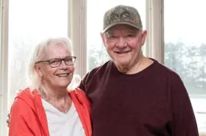 A senior couple poses in their home, smiling at the camera.