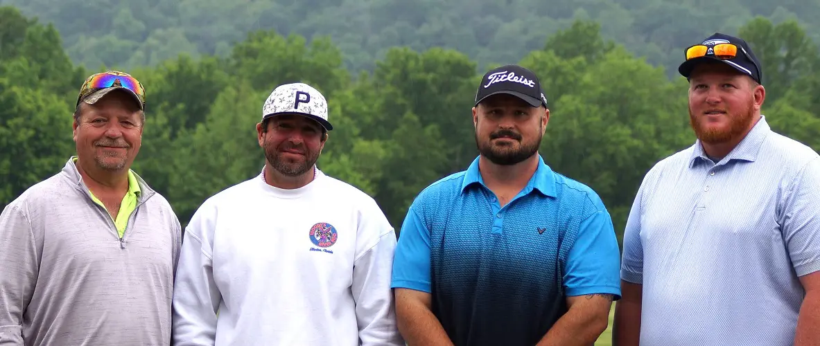 Four male golfers pose for a picture on a golf course.