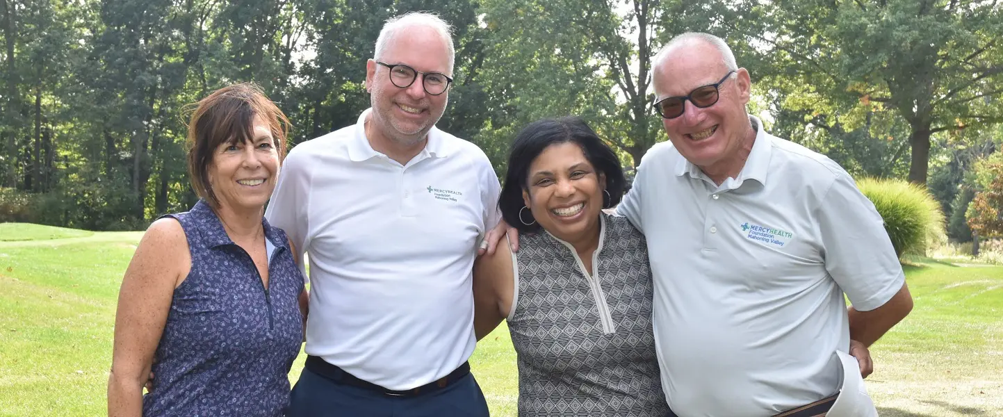 A group of smiling, professional adults pose for a picture on a golf course.