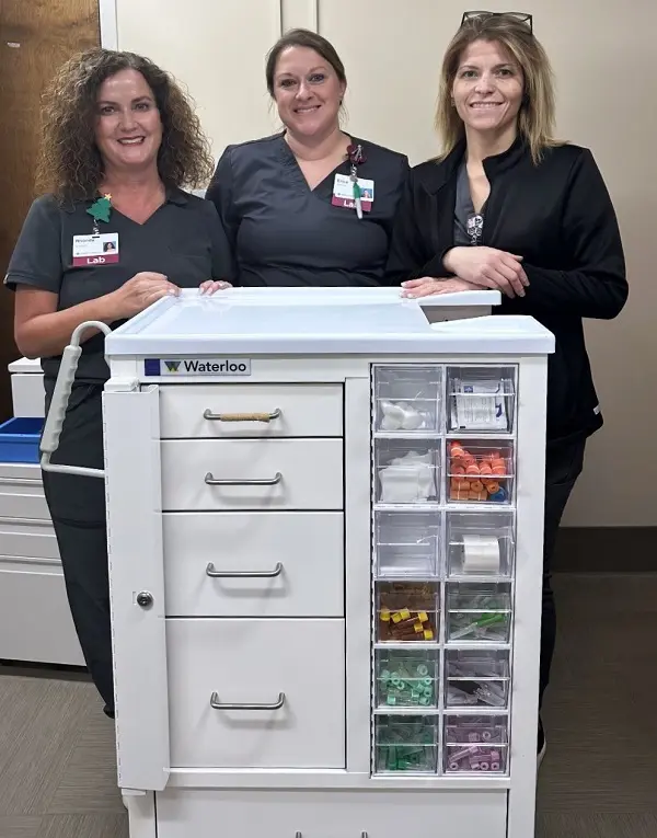 Three lab staff members at Mercy Health - Marcum and Wallace Hospital pose with a new phlebotomy cart.