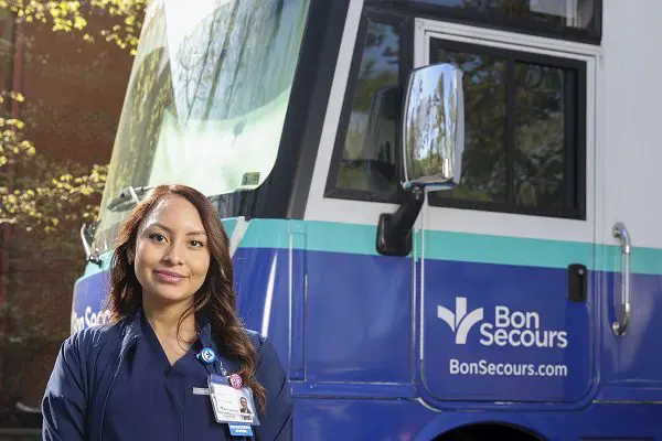 A young woman in dark blue scrubs stands outside the Bon Secours Richmond Care-A-Van mobile health coach.