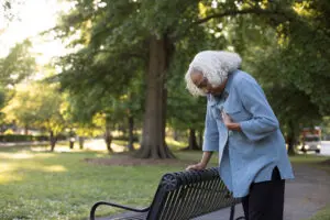 Elderly woman leaning onto park bench while holding her chest