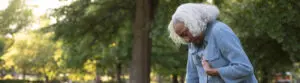 Elderly woman leaning onto park bench while holding her chest