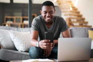 Shot of a young man using a cellphone and laptop at home.