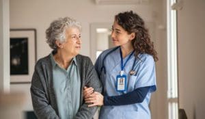 Young caregiver helping senior woman walking. Nurse assisting her old woman patient at nursing home. Senior woman with walking stick being helped by nurse at home.