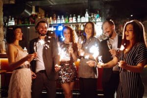 Glowing sparkles in hands. Young friends celebrate new year and holding bengal lights and glasses with drink. Winter holiday, youth, party, lifestyle concept.