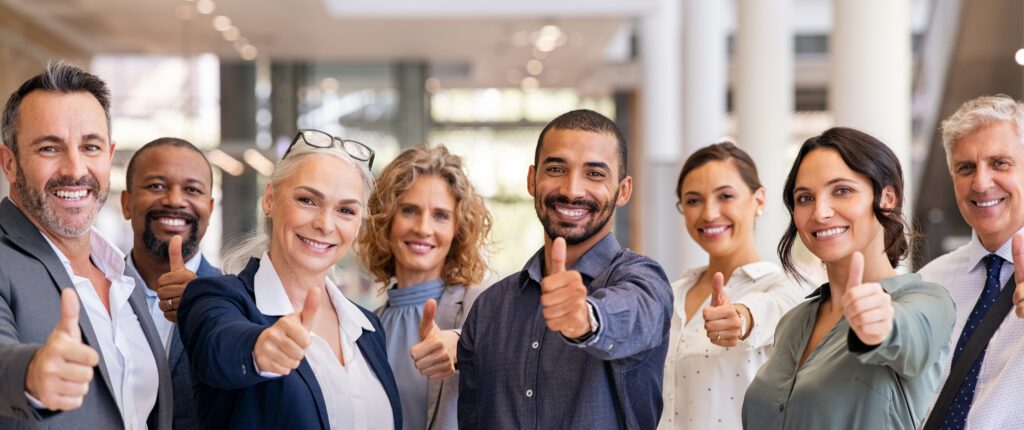 Group of happy multiethnic business people showing sign of success. Successful business team showing thumbs up and looking at camera. Portrait of smiling businessmen and businesswomen cheering at office.