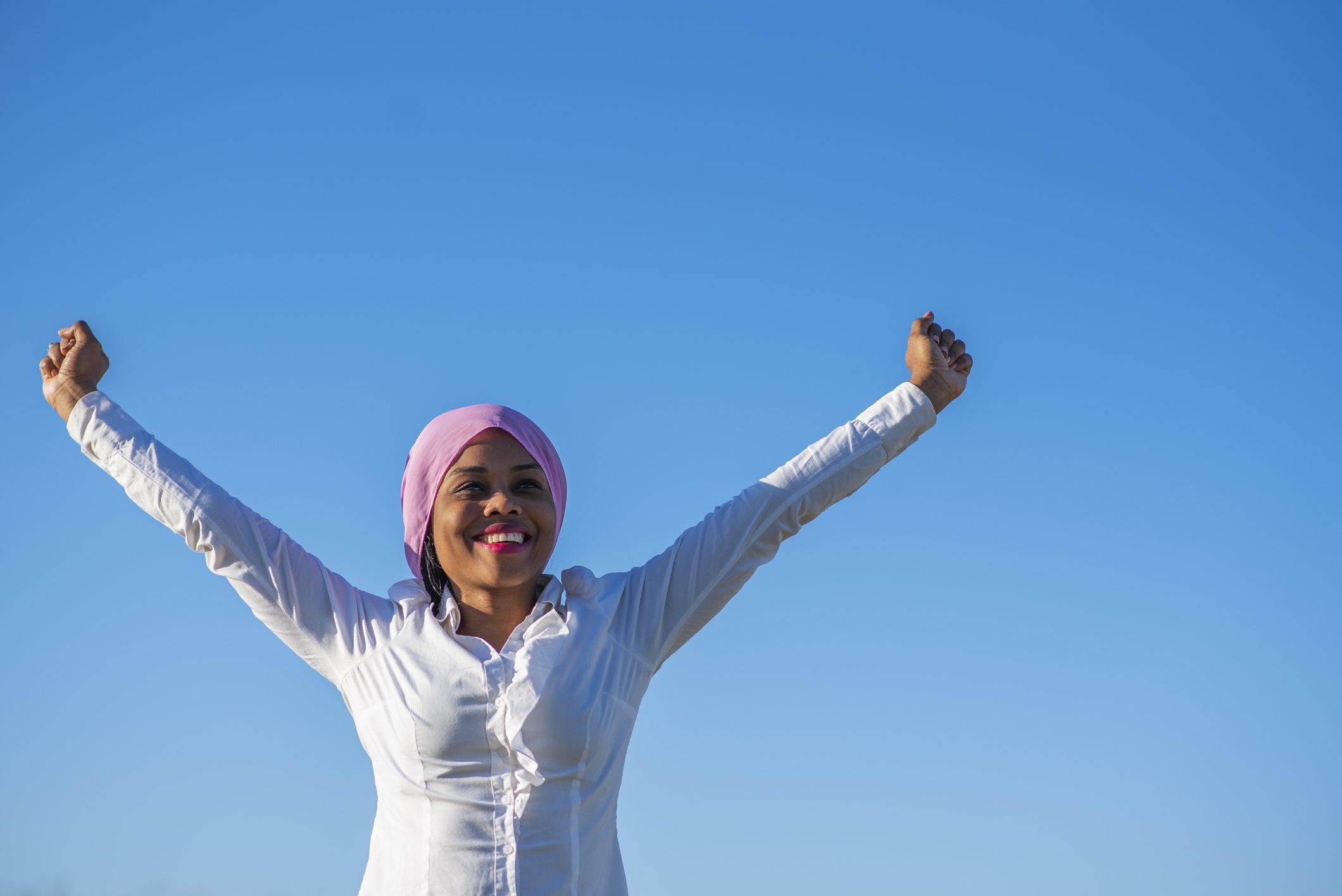 Very smiling African-American woman with a pink headscarf raising her arms