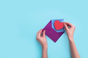 A female hand opens an envelope with a red heart on pink background.