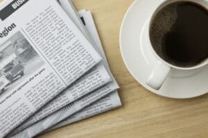 A newspaper and a cup of coffee on a wooden table, shot directly from above.