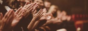 Side view of smiling spectators clapping hands in auditorium.