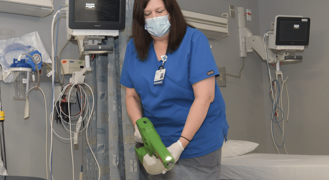 A cleaning services staff member uses a special mister to disinfect a hospital room.