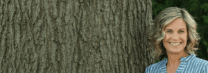 A young woman stands beside a great big tree outside.