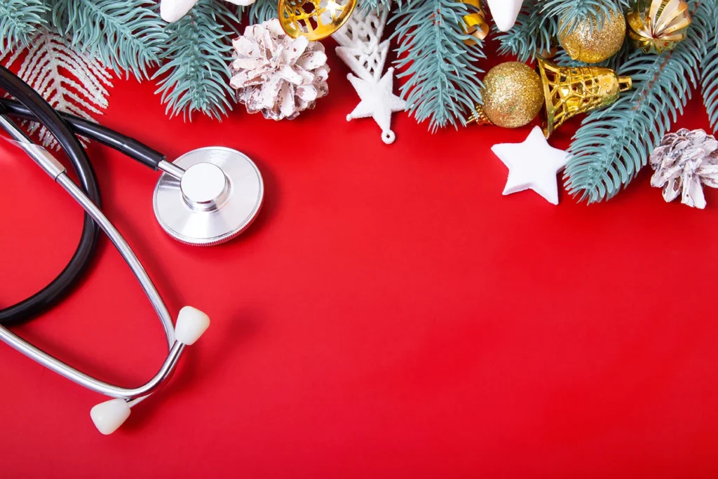 Festive winter holiday decor and a stethoscope are laid together against a red background.