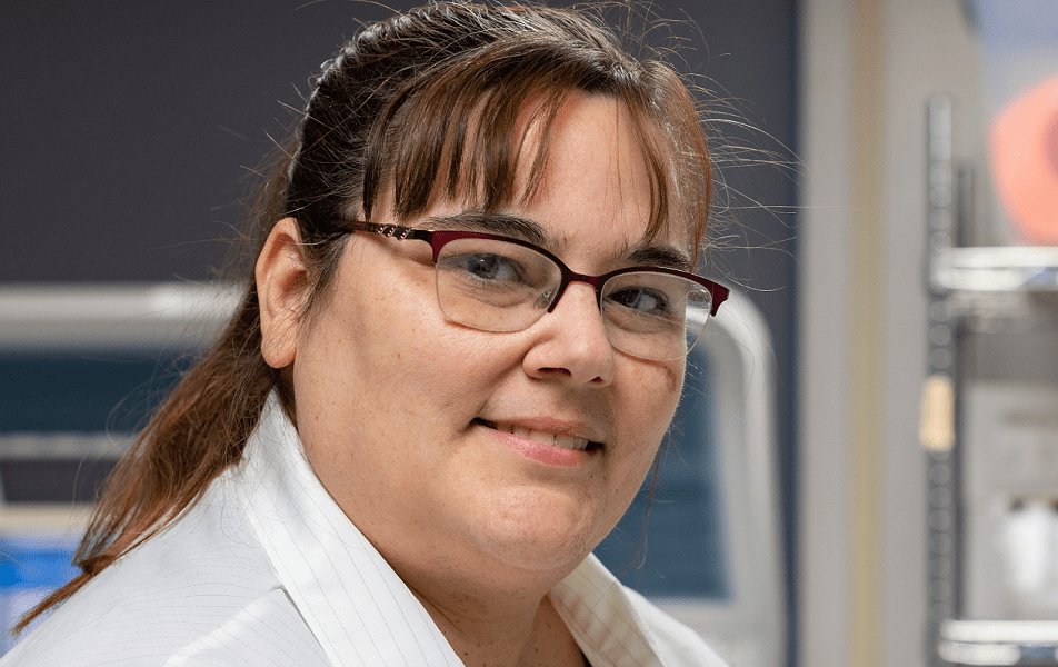 Regina Queen, a lab supervisor at Mercy Health Urbana Hospital, smiles in her lab. She is a middle-aged white woman with a brunette pony tail and glasses.