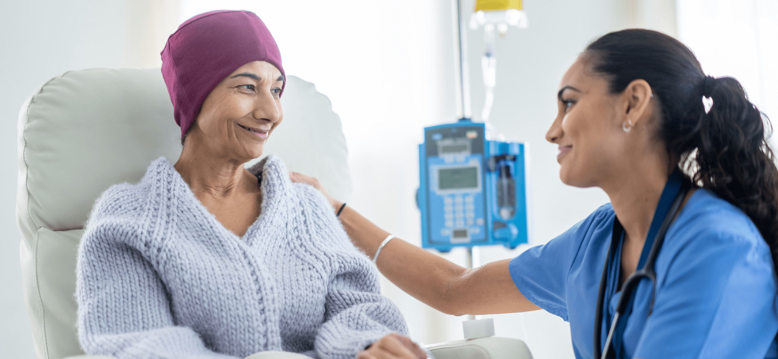 A young female cancer patient smiles at her nurse while receiving a transfusion.