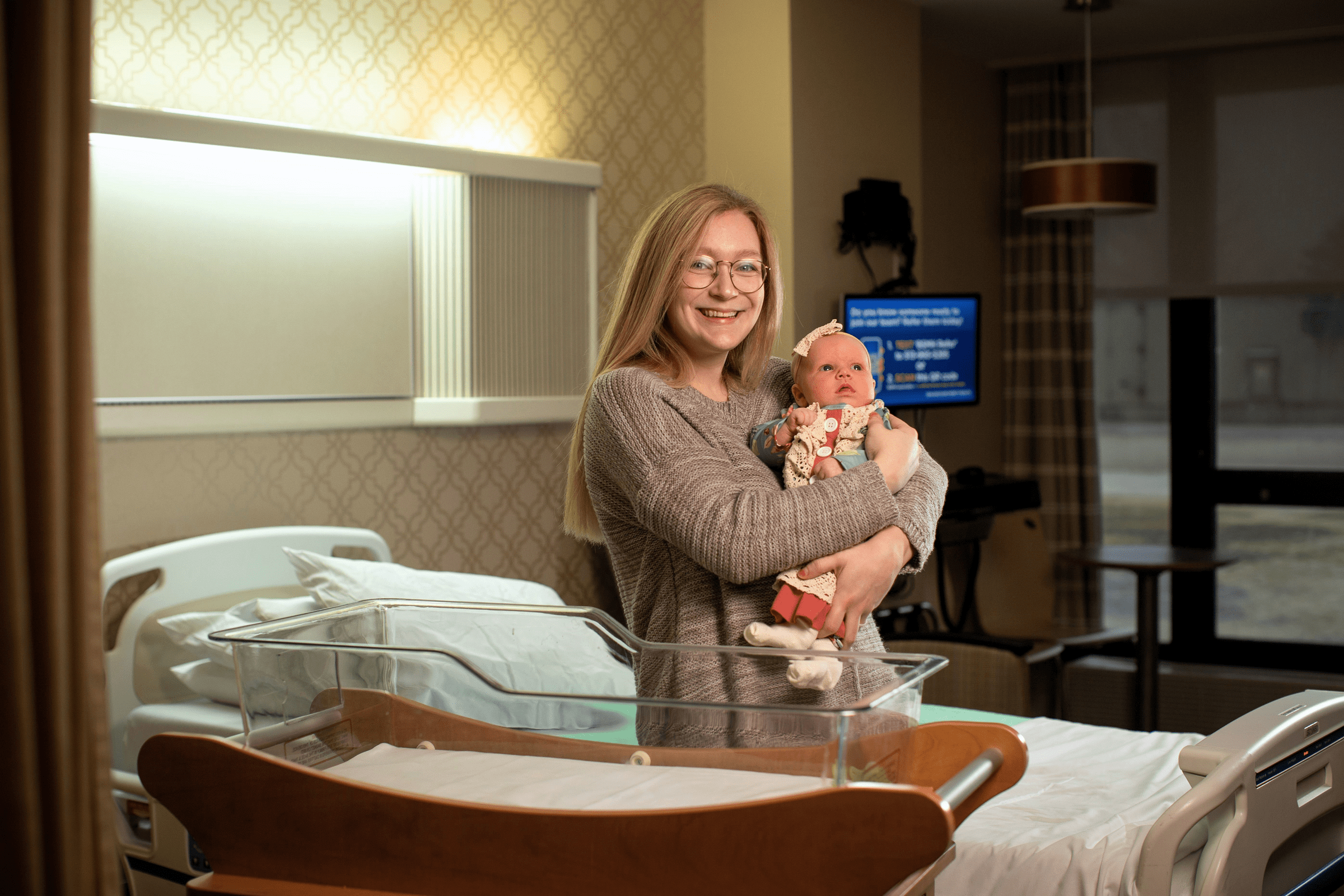 A young mom smiles while holding her newborn baby in her patient room at Mercy Health Lourdes Little Miracles Birthing Center.