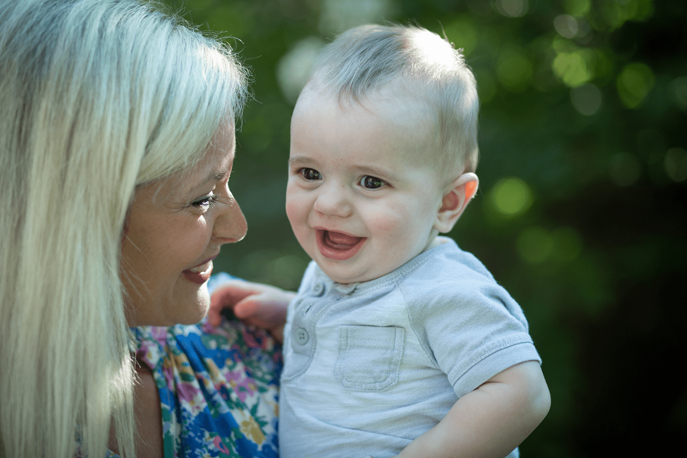 A young, blond mom smiles at her young baby, who she is holding.