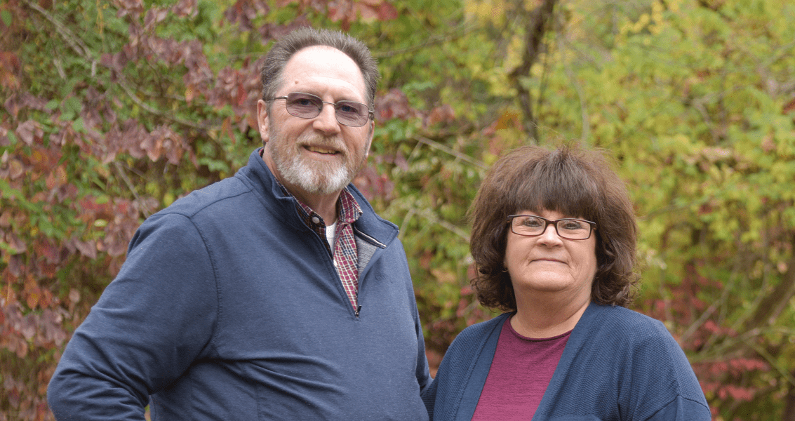 A man and woman stand outside on an autumn day.