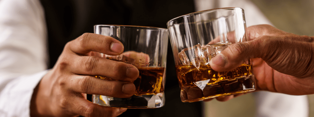 Two men cheers rocks glasses of bourbon.