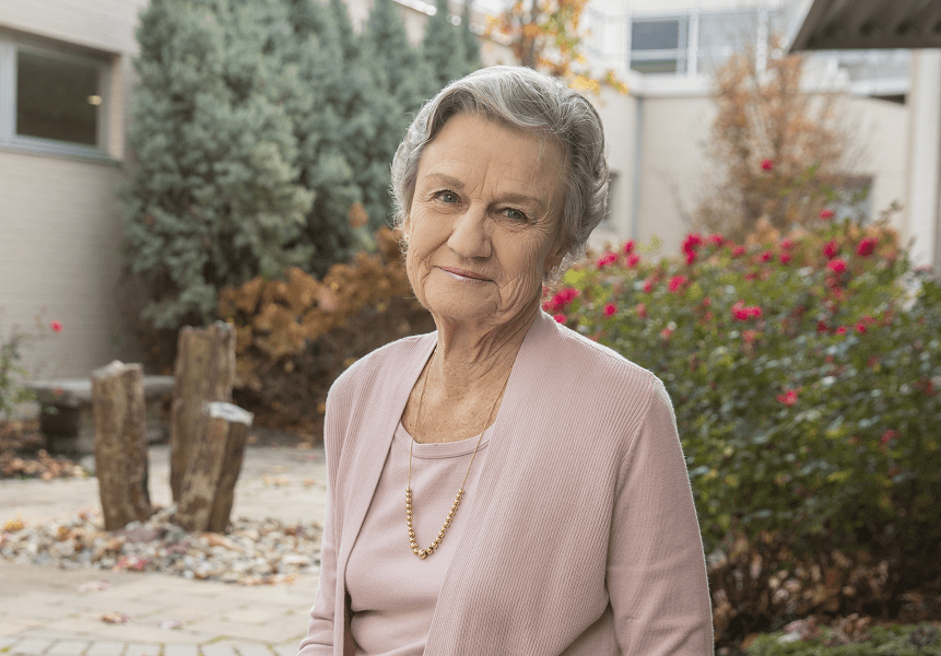 An elderly woman sits in a court yard in the fall.