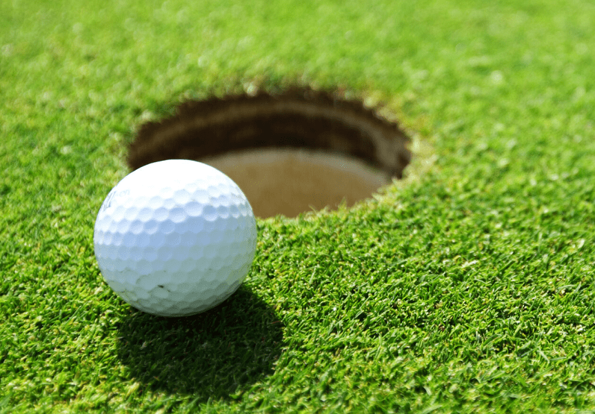 A golf ball sits on the green right beside a hole.