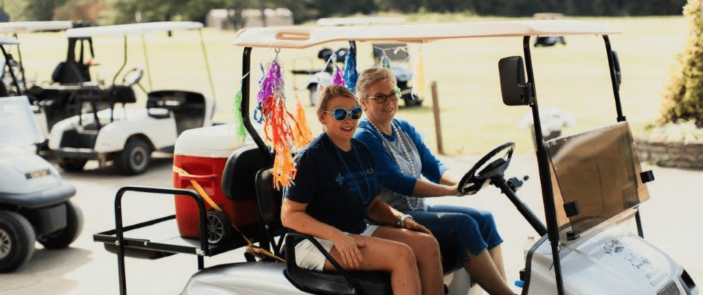 Two women cruise on a golf cart at Mercy Health Foundation Irvine's Annual Golf Scramble.