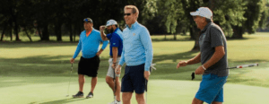 A group of men laugh while walking a golf course.