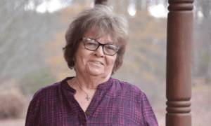 An older woman stands outside on a fall day.