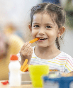A little girl is eating a carrot.