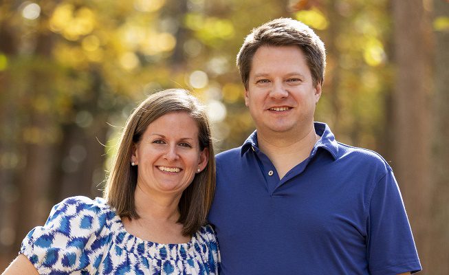 A young couple stands outside in the woods on a sunny day.