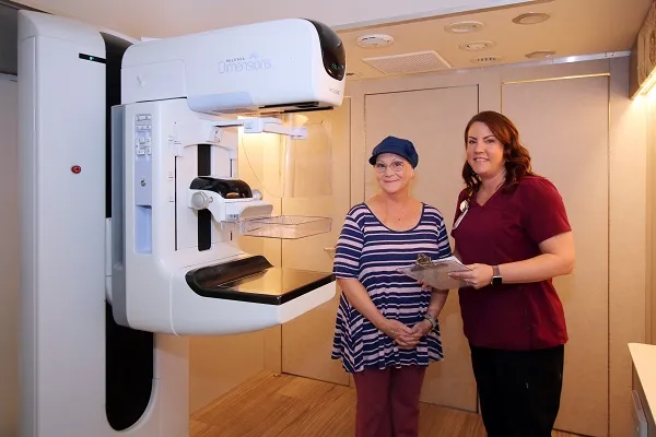 A patient stands with a nurse inside a mobile mammography coach, next to the mammography machine.