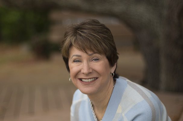 A middle-aged woman sits underneath a big tree, smiling.