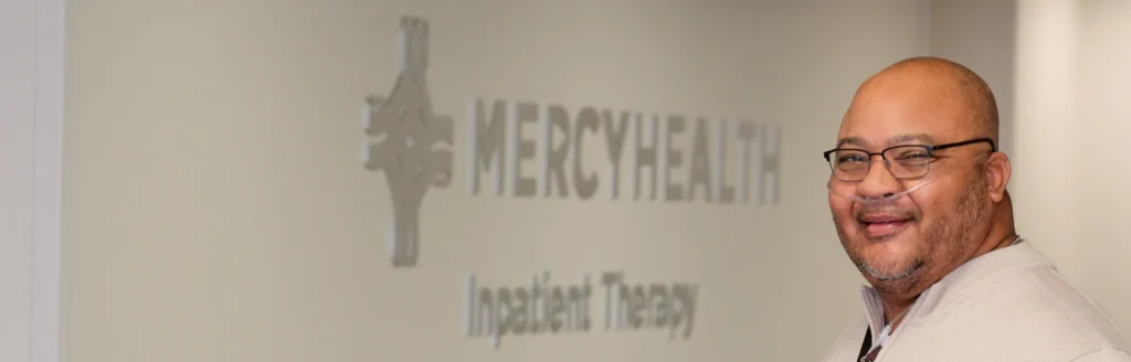 A smiling man stands in front of a Mercy Health Inpatient Therapy sign.