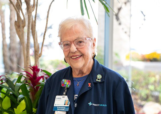 An elderly woman volunteers at the reception desk of a hospital.