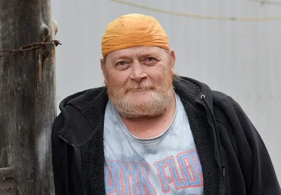 An elderly man in an orange cap stands outside.