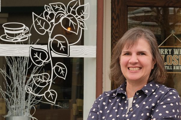 A middle-aged woman stands outside the storefront of a local coffee shop.