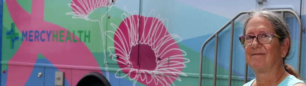 An elderly woman stands outside of a Mercy Health Mobile Mammography Van, which is decorated with flowers.