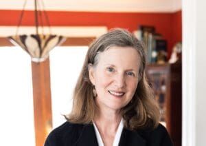 An older woman smiles while standing in a doorway of her house.
