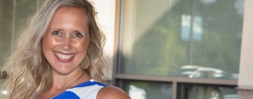 A blonde woman in a blue and white print dress stands outside.