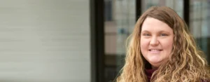 A young woman stands outside an office building, smiling at the camera.