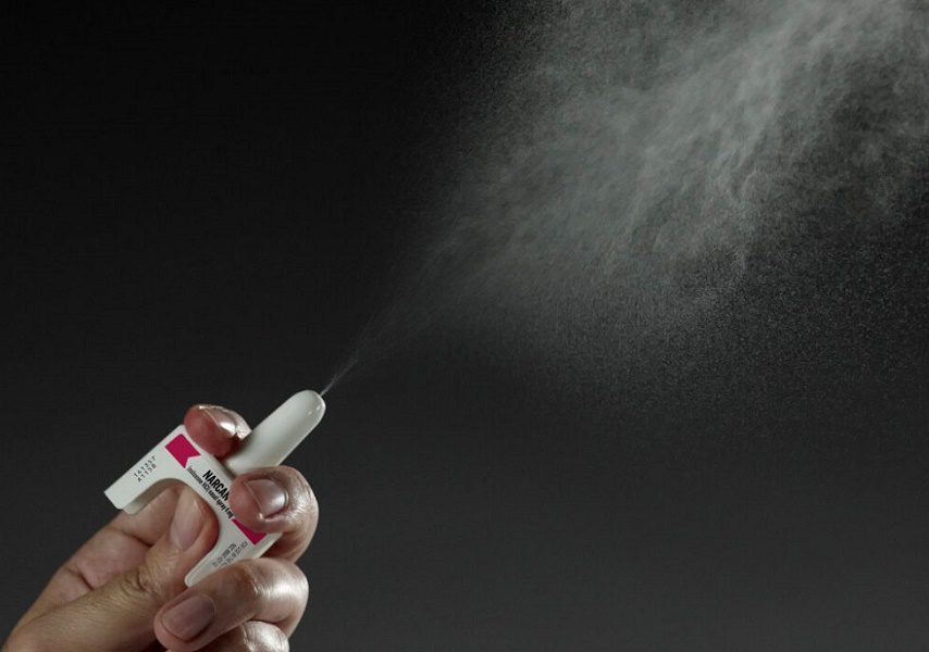 A hand spraying a dose of naloxone nasal spray.