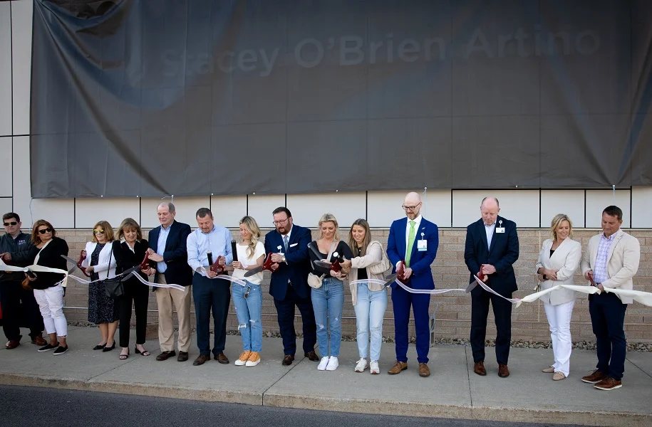 People with pairs of giant scissors stand in a line to cut a big ribbon.